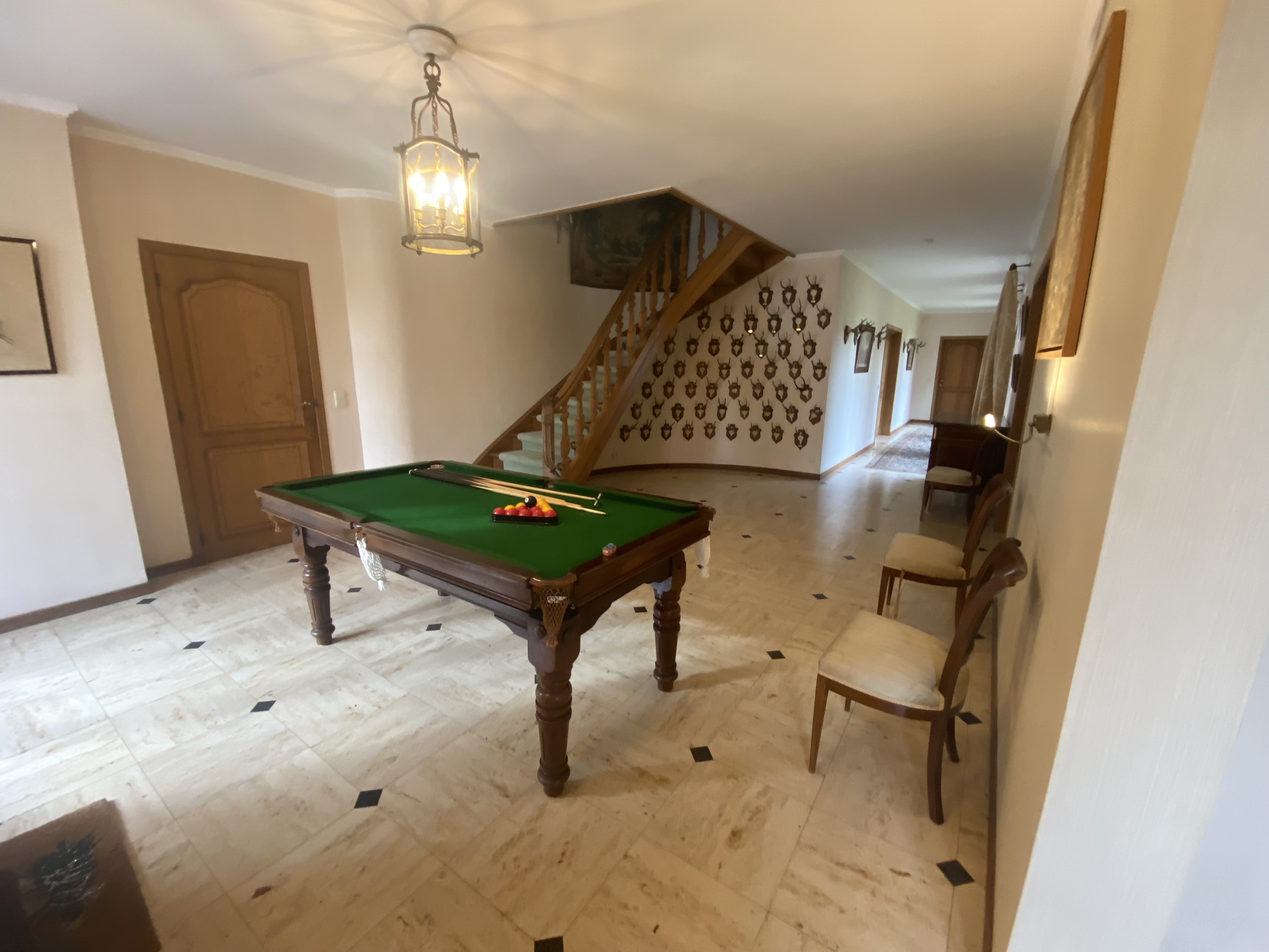 Salle de billard avec table en bois, escalier et trophées de chasse