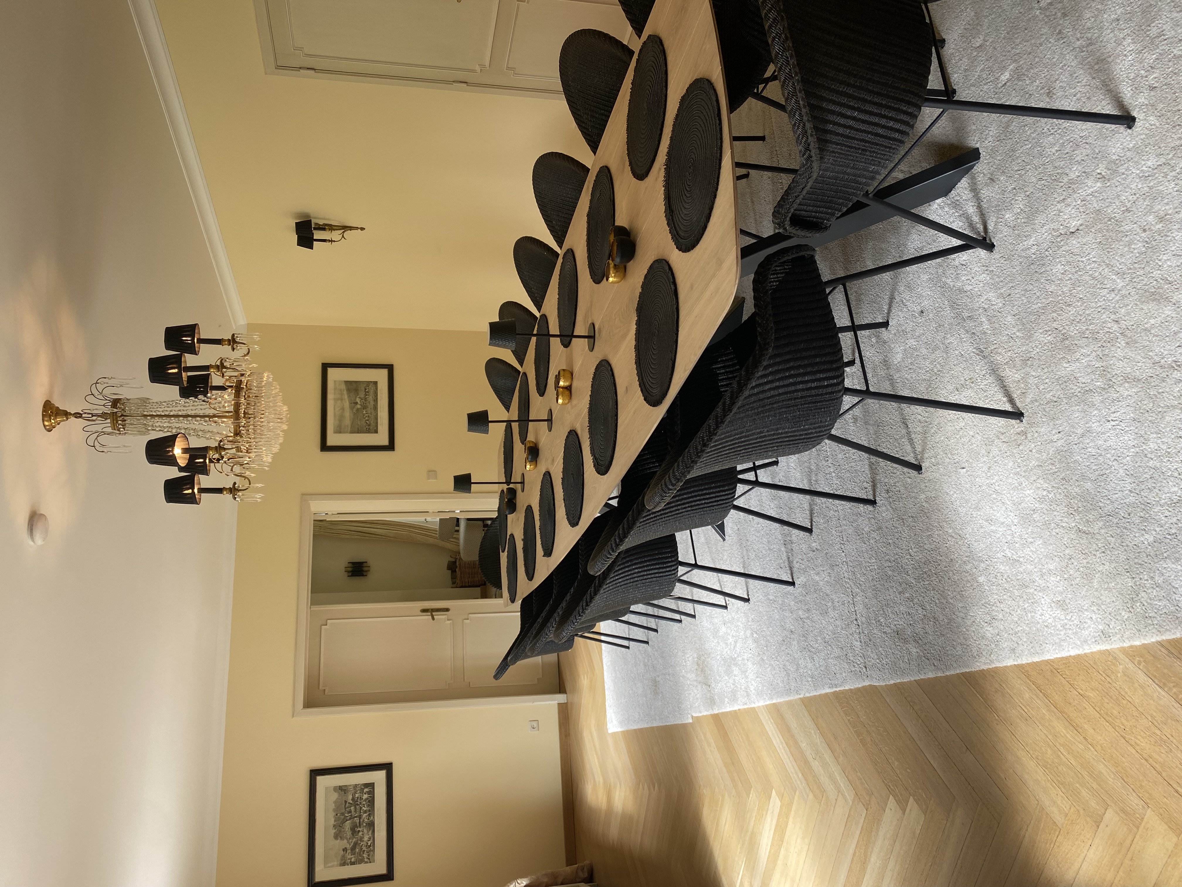 Grande salle à manger avec longue table en bois, chaises noires et lustre en cristal