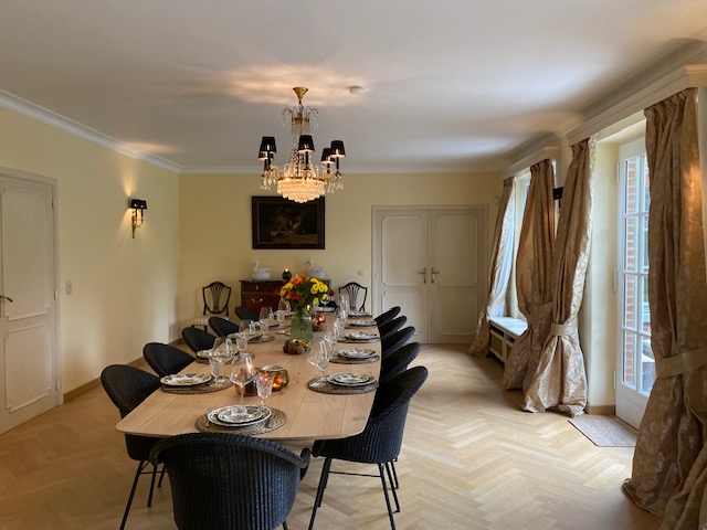 Grande salle à manger avec table en bois, lustre en cristal et parquet en chevrons