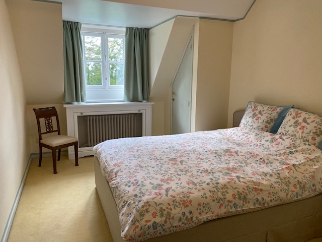 Chambre mansardée avec lit double, parure florale et rideaux verts