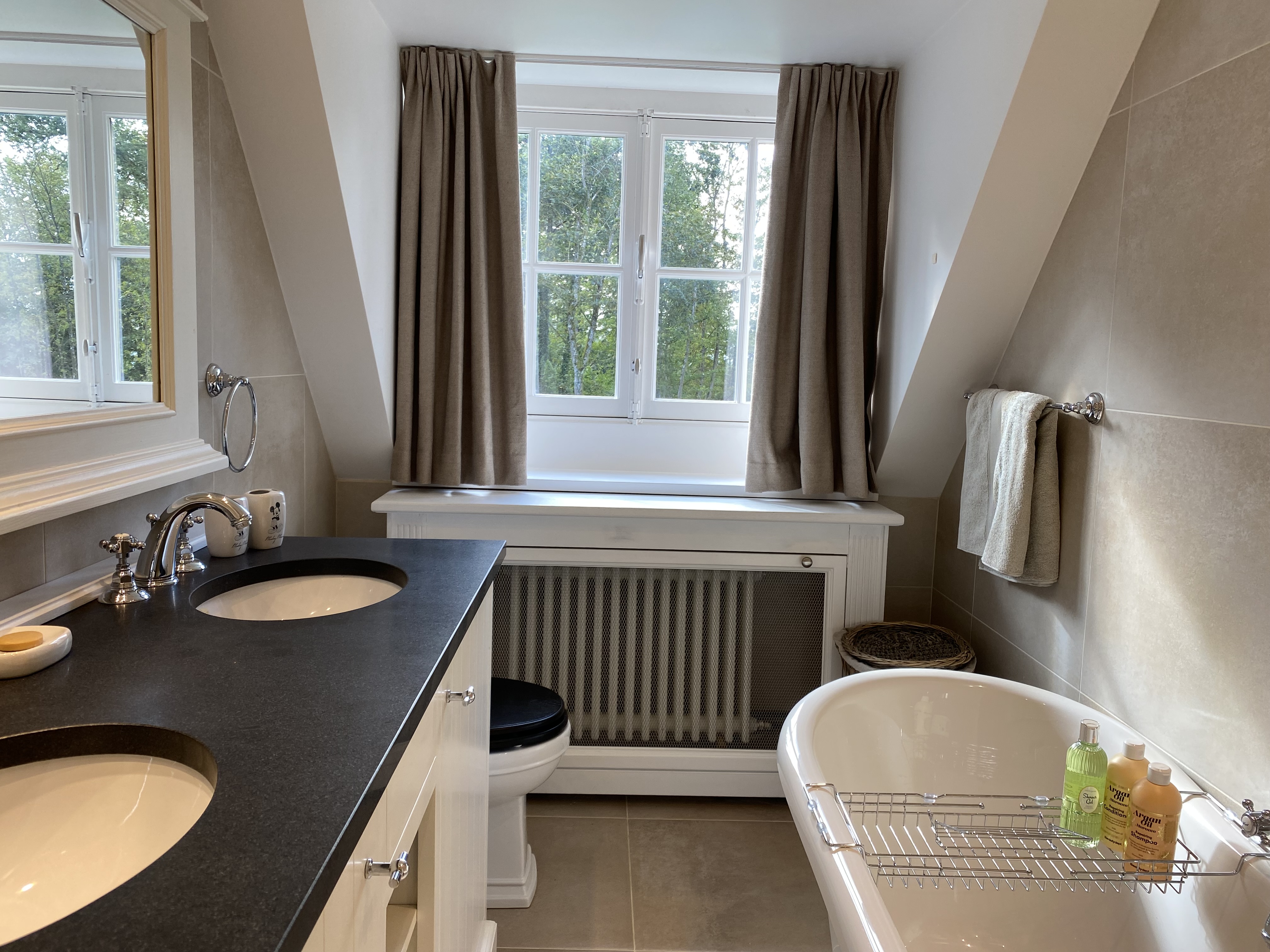 Salle de bain lumineuse avec double vasque, baignoire îlot et vue verdoyante